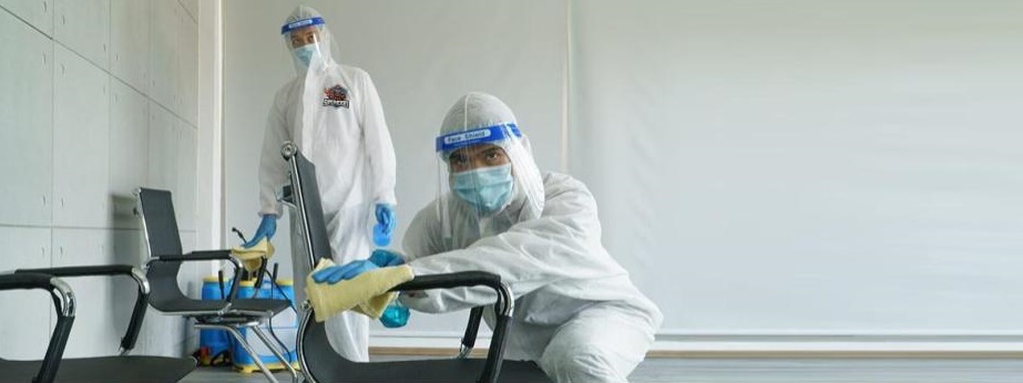 Two professionals in protective gear cleaning and sanitizing surfaces in an indoor environment, emphasizing environmental remediation and safety after contamination.
